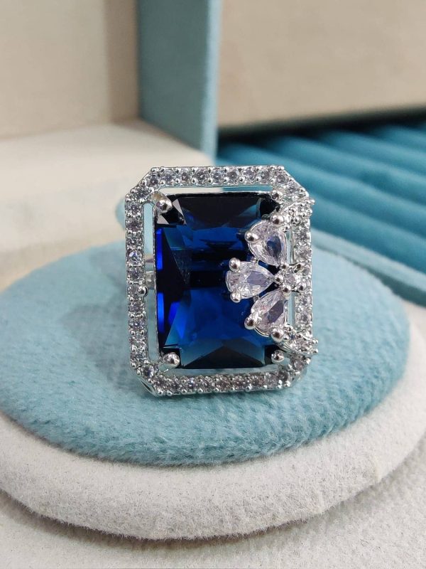 Branded deep sapphire blue colour American diamond solitaire ring with a base metal of brass and oxidised silver plating presented on a round sky blue cloth bed.